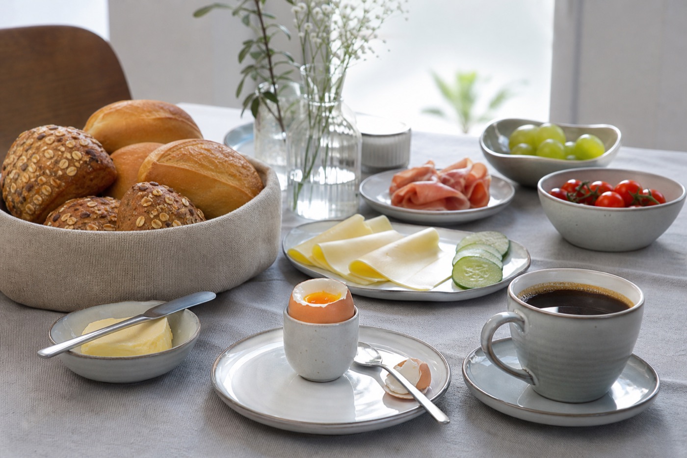 A German breakfast table with bread rolls, butter, cheese slices, a soft-boiled egg in a cup and a cup of coffee